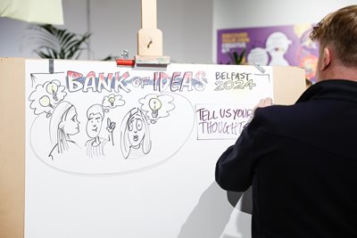 Person writing on a flipchart pad and submitting an idea to the 'Bank of Ideas'.