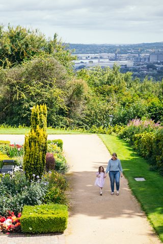 A girl and woman take a walk in the castle gardens with Belfast in the background.