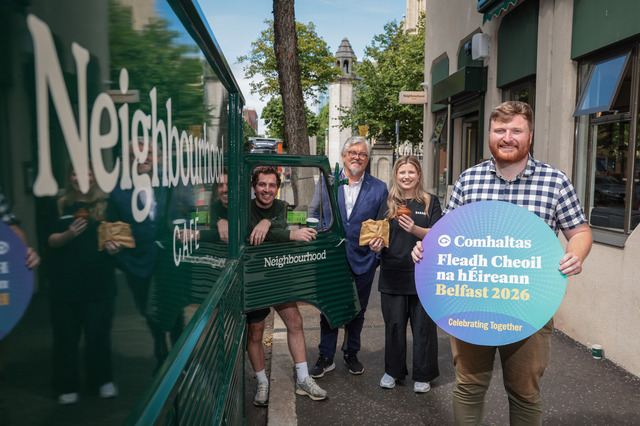 Four people including Councillor Conor McKay standing on street in city centre - beside a mobile van and cafe. Cllr McKay holds sign promoting the 2026 Comhaltas Fleadh Cheoil na hÉireann .