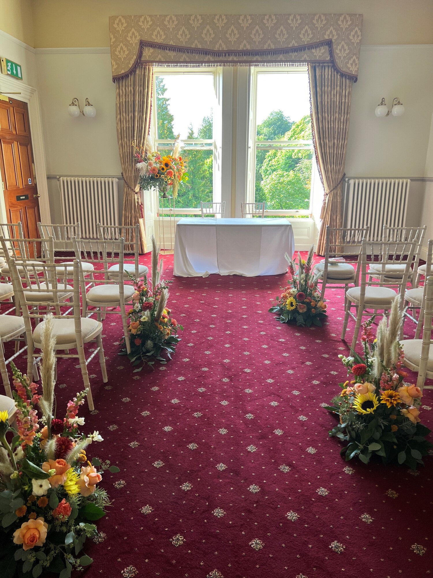 Ashley Room set up for a wedding in a Theatre style with chairs dressed with flowers on either side of an aisle.