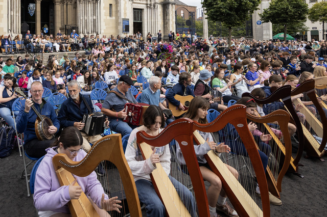 Students and their tutors gathering on the steps of Belfast Cathedral for Seisiún Mór na hÉigse, a massive collaborative performance filling the city with traditional music.