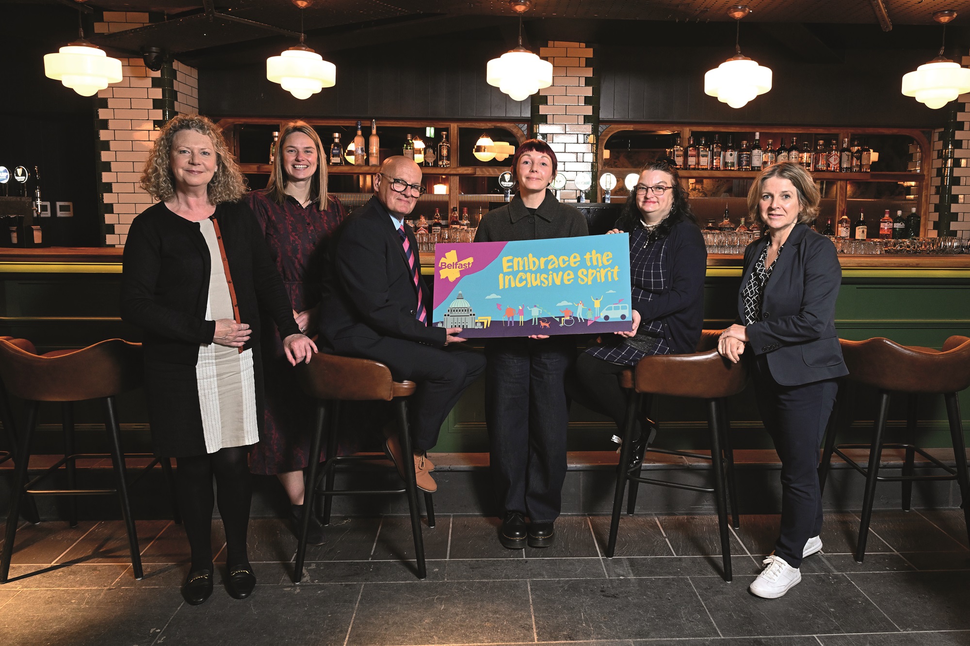 Representatives from Tourism NI, Visit Belfast, Belfast City Council and Open Arts holding a prop to highlight the Embrace the Inclusive Spirit programme. 