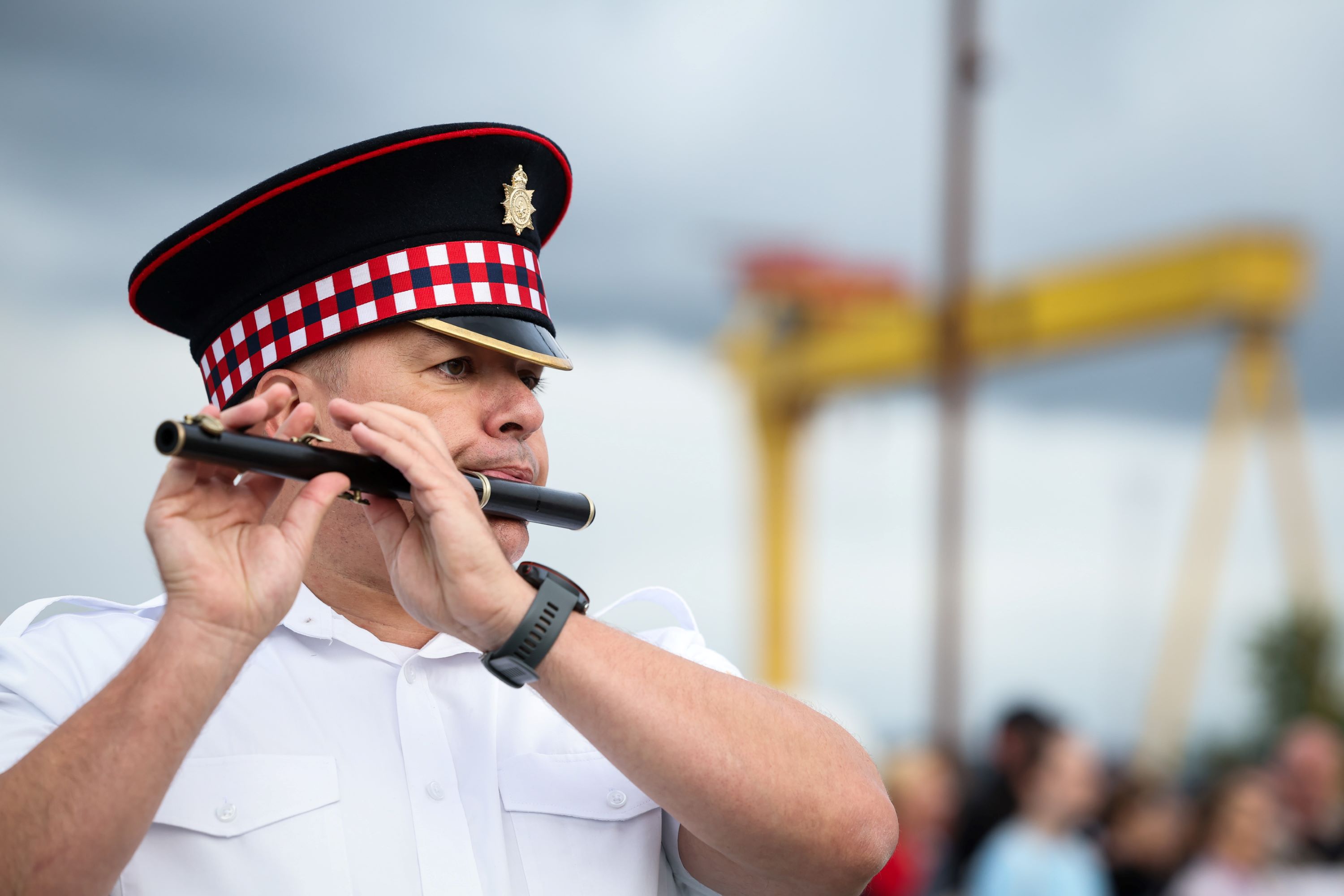 Flute band member playing flute against backdrop of Harland and Wolff cranes