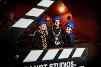Patricia Corbett (The National Lottery Heritage Fund), Lord Mayor of Belfast, Councillor Micky Murray, and Mimi Turtle (Strand Arts Centre), dressed in hard hats with film clapperboard in foreground.