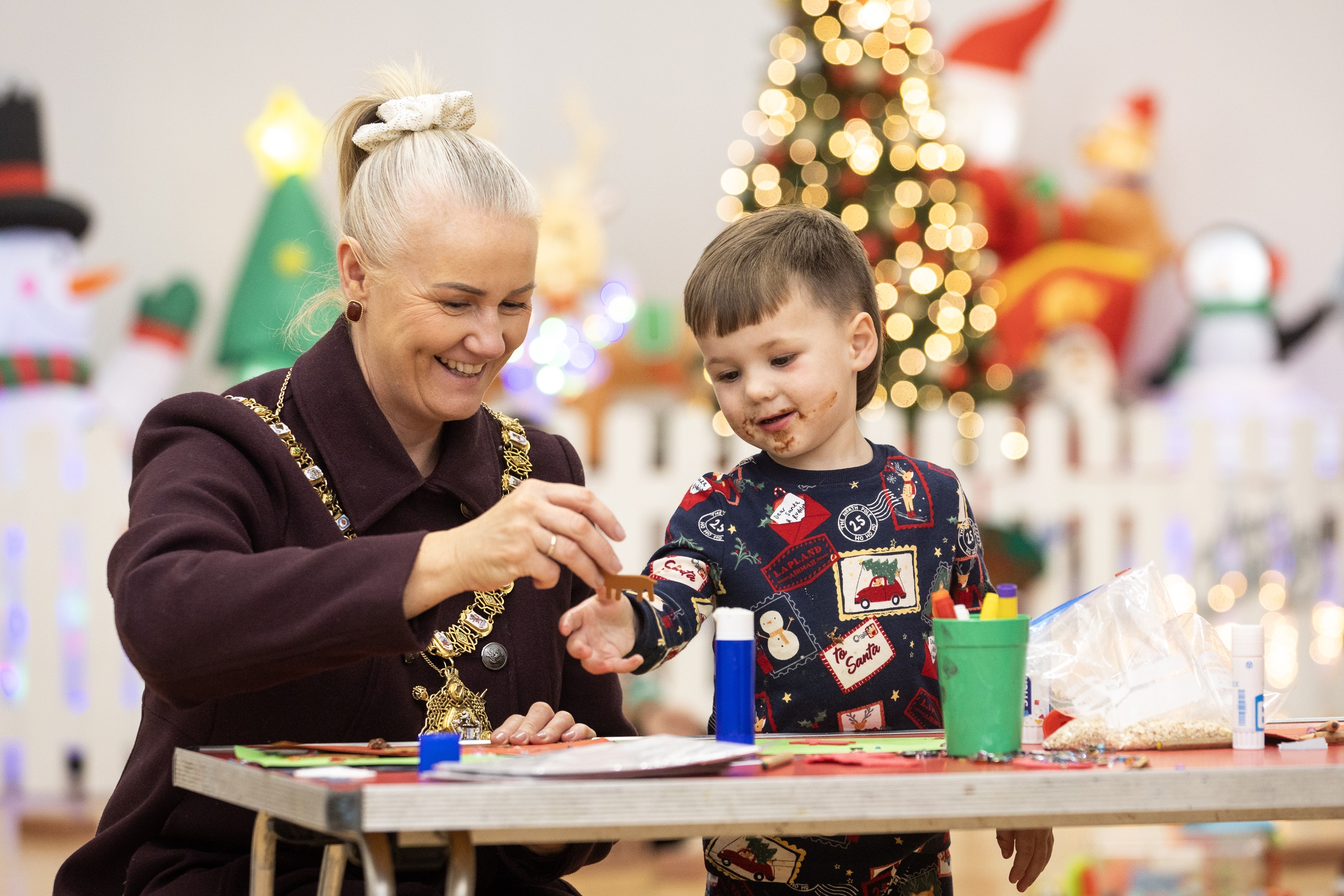 Lord Mayor and little boy play together at a table with a Christmas tree in the background 