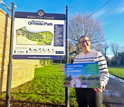Councillor Ruth Brooks beside an Ormeau Park sign holding a photo prop promoting the park opening hours consultation