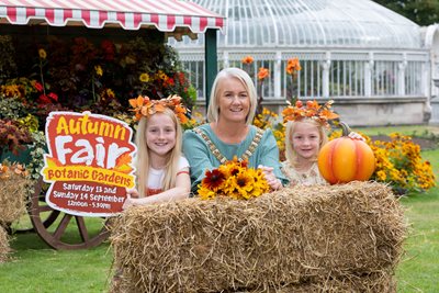 Lord Mayor Councillor Tracy Kelly and two young girls behind a hay bail and in front of a floral display with Autumn Fair photo props