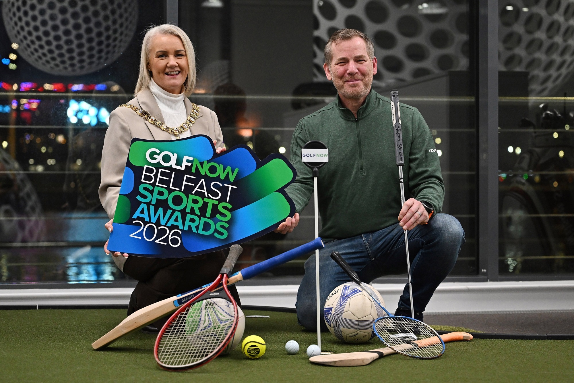 Lord Mayor of Belfast, Councillor Tracy Kelly, joins Brian Smith from GolfNow to launch the GolfNow Belfast Sports Awards 2026, holding a range of sporting equipment props.