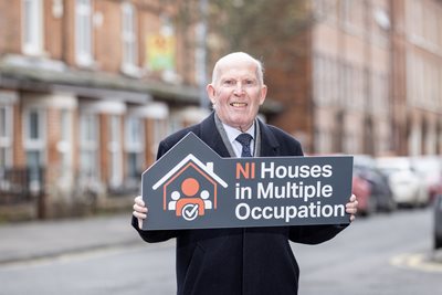 Alderman Jim Rodgers, Chair of Belfast City Council's Licensing Committee, holds up a sign advertising NI HMO legislation.
