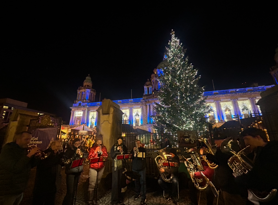 Brass band performing outside City Hall, with Christmas tree in the background.