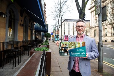 Councillor Gary McKeown holds a poster promoting the  pavement café licensing scheme consultation - on a pavement in the city centre.