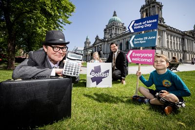 Deputy Lord Mayor of Belfast, Councillor Paul Doherty, ‘bank manager’ Stephen Beggs and Caleb and Hanna Bateson carry colourful props to highlight the Bank of Ideas on lawns of City Hall.