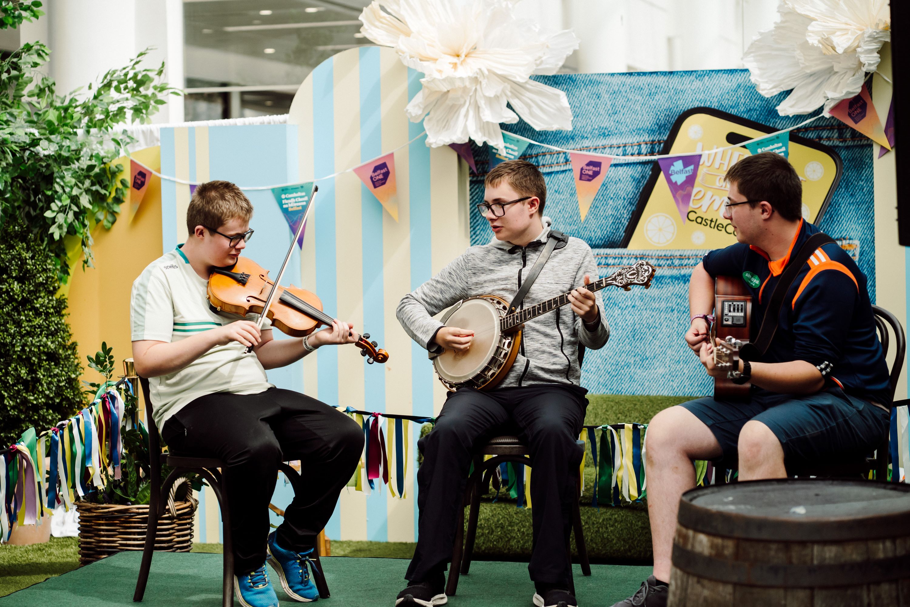 Three boys play musical instruments sitting outside on chairs