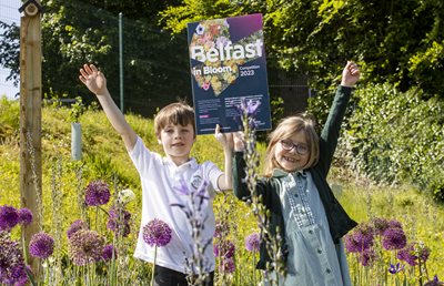Two pupils from Dundela Infants School hold a Belfast in Bloom 2023 poster in the school's wildflower garden