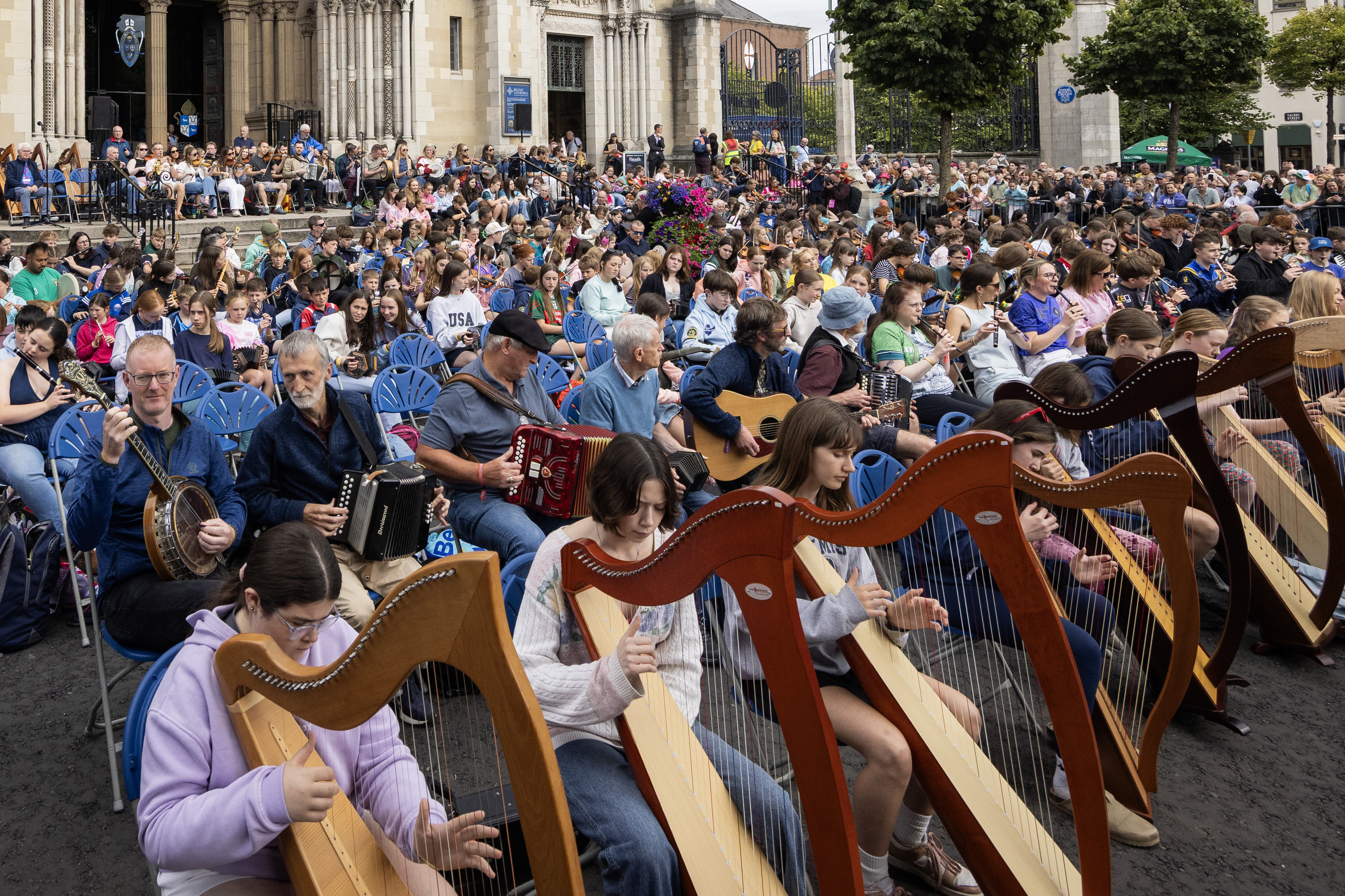 Students and their tutors gathering on the steps of Belfast Cathedral for Seisiún Mór na hÉigse, a massive collaborative performance filling the city with traditional music.