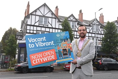 Lord Mayor of Belfast, Councillor Micky Murray, holding up a sign advertising Vacant to Vibrant scheme on Lisburn Road, Belfast.