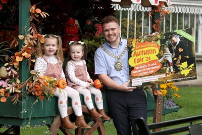 Two children in autumnal dress with the Lord Mayor who holds an Autumn Fair event poster