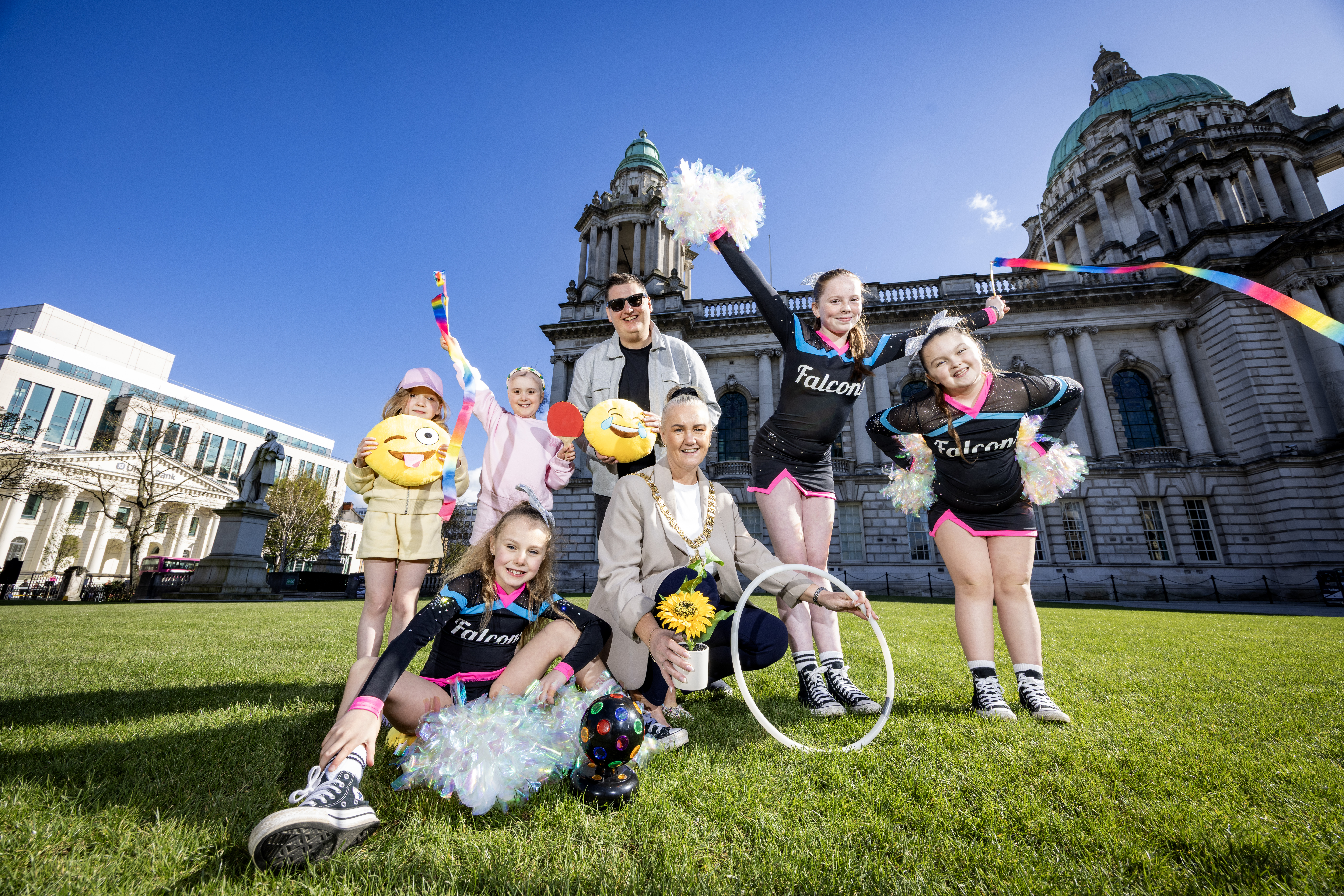 Kids on City Hall lawn with Lord Mayor and Stuart Robinson, holding colourful props against a sunny sky.