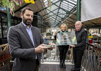 Councillor Gareth Spratt holds an award to recognise St George's Market being named Best Large Indoor Market in the UK. He is with two traders at the market.