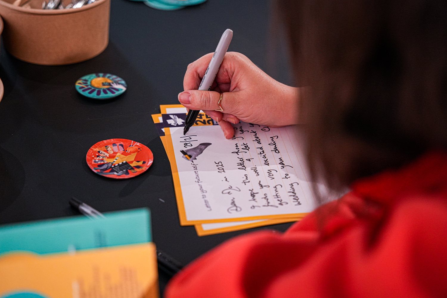 A female hand writing a letter on a colourful piece of paper with Belfast 2024 branding