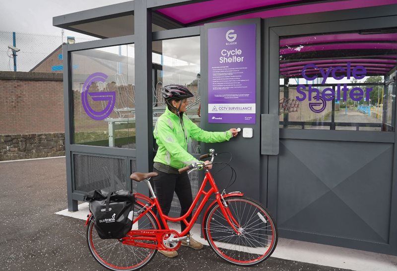 Female cyclist using a key fob to access secure cycle storage at a Glider halt in Belfast.