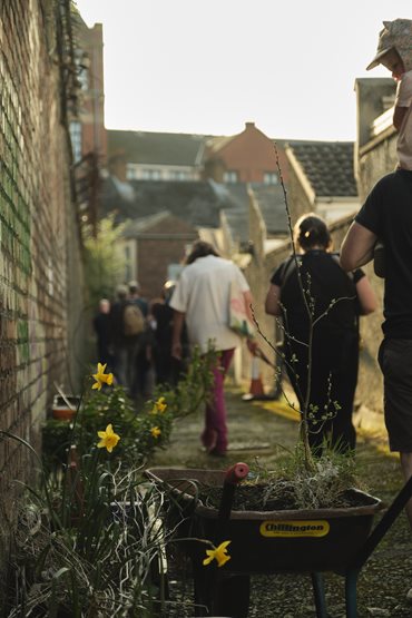 People walking down an alleyway with flowers in the foreground