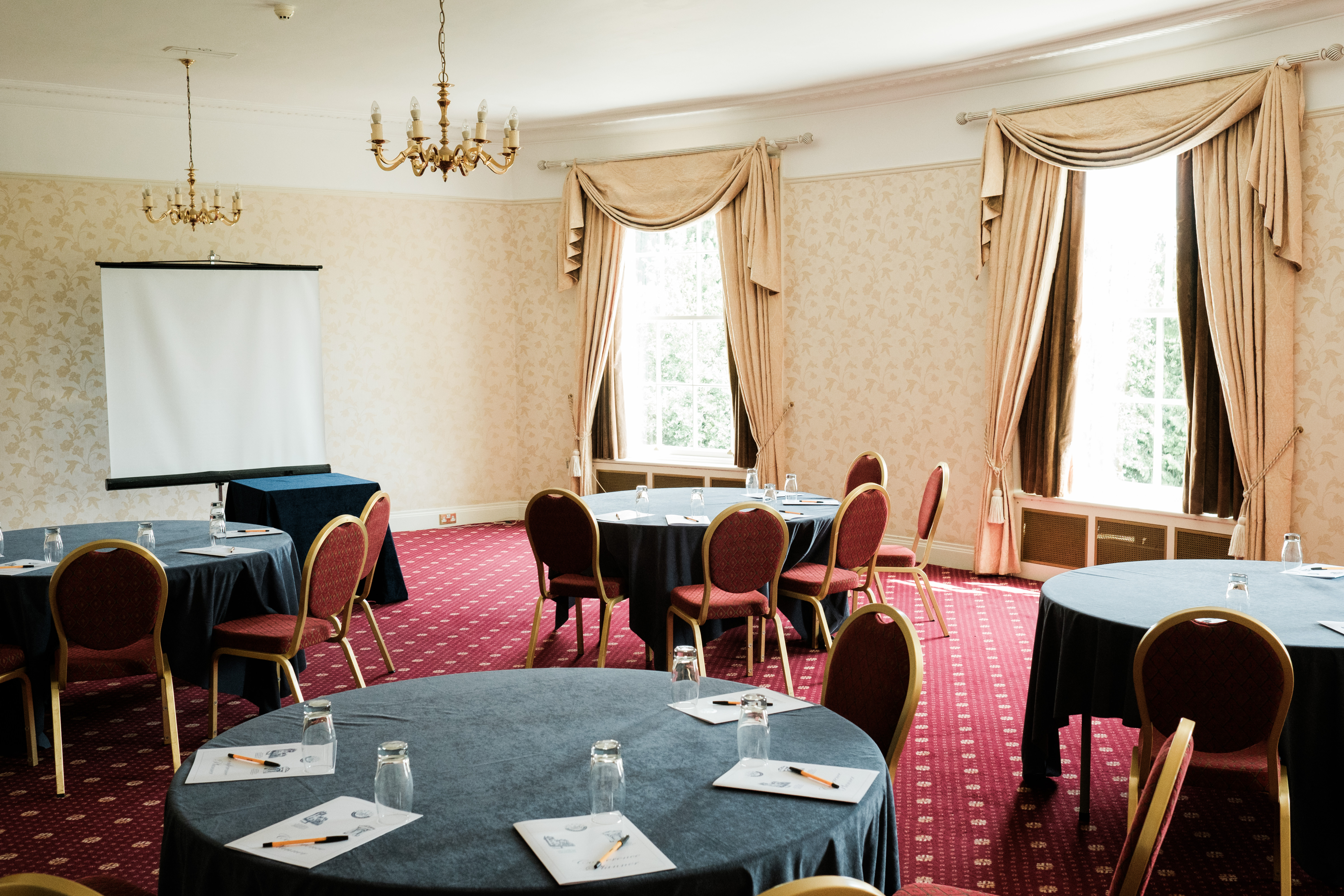 Circular tables set up in a Cabaret style in the Hilsborowe Room facing a screen for a presentation.