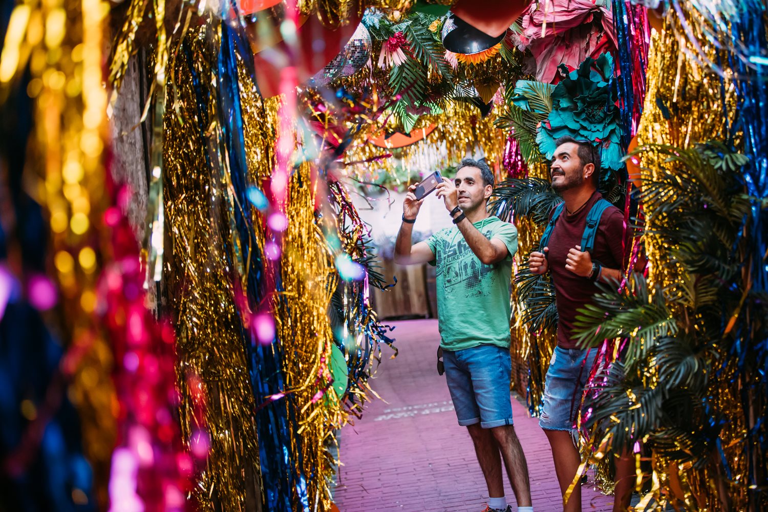 Two men taking photographs in an alleyway surrounded by colourful tinsel