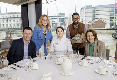 Belfast Lord Mayor Councillor Tina Black with a group of people at a table set for dinner overlooking the River Lagan from the ICC in Belfast.