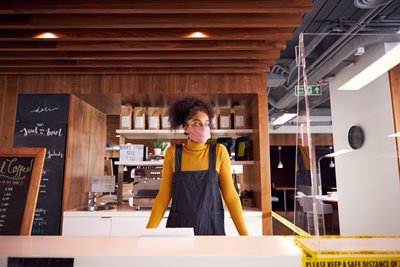 Counter service assistant wears face covering and stands behind counter in a cafe