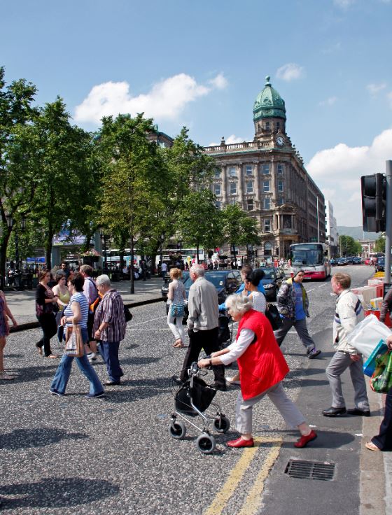 Group of people of all ages crossing the road outside City Hall in Belfast city centre.