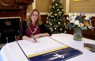 Belfast Lord Mayor Councillor Tina Black sits at a desk, signing the White Ribbon Charter.
