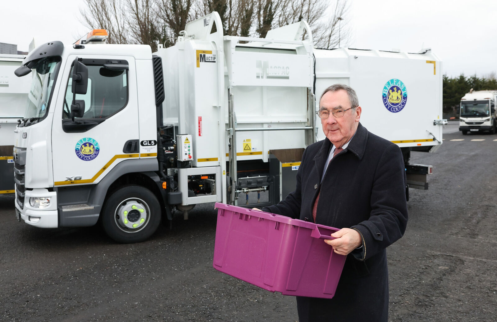 Councillor Fred Cobain, Chair of the People and Communities Committee holding a purple glass recycling box in front of a glass recycling vechicle.