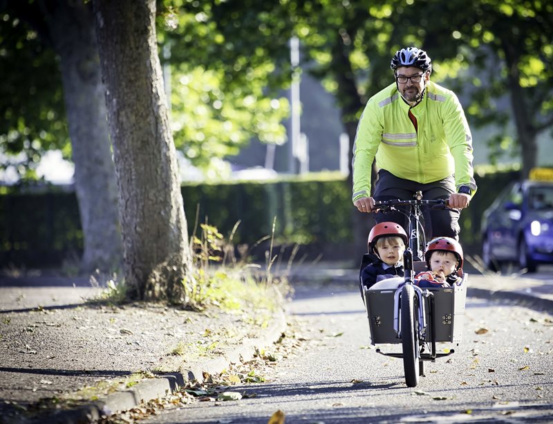 Man cycling with two young children in a cargo bike.