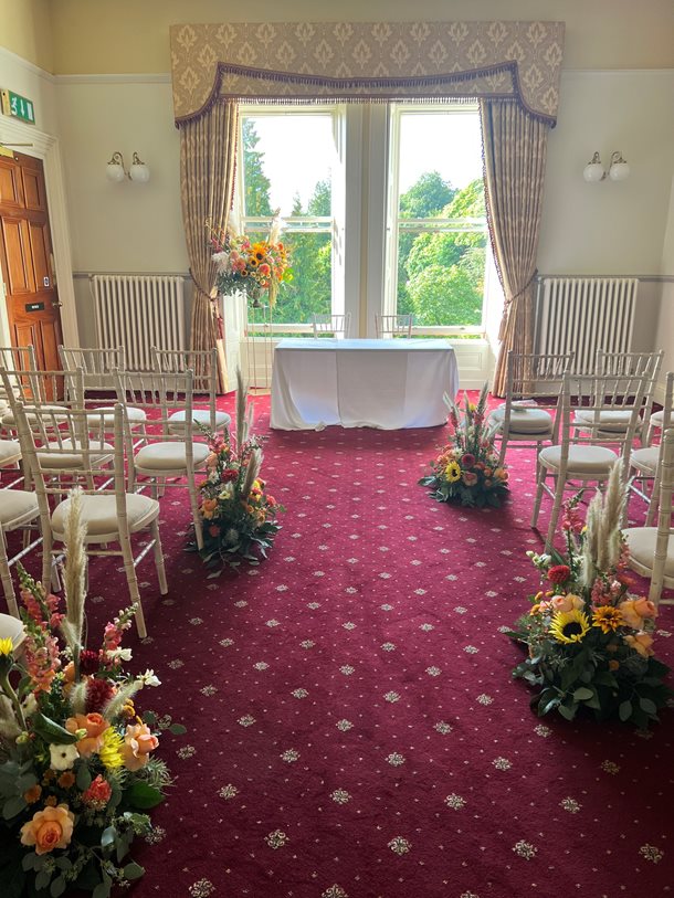 Ashley Room set up for a wedding in a Theatre style with chairs dressed with flowers on either side of an aisle.